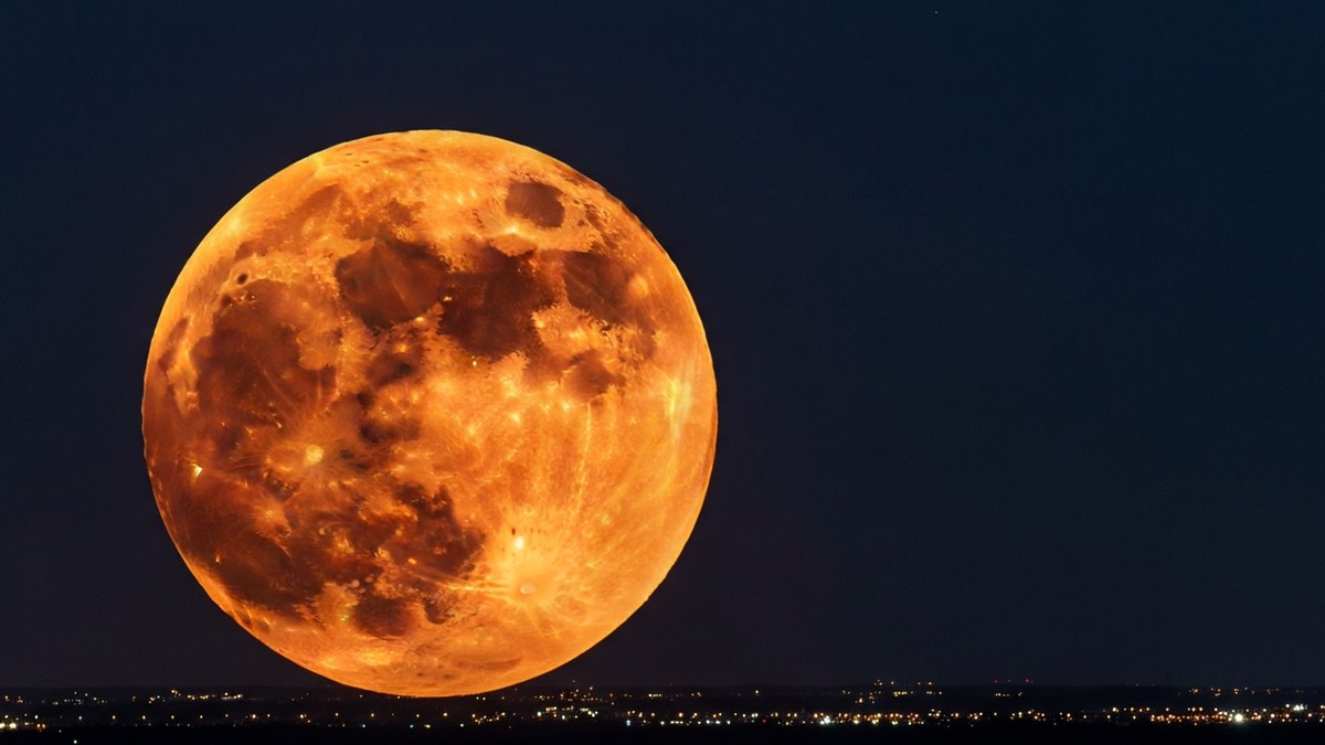 A large glowing orange Moon low over a city skyline at night