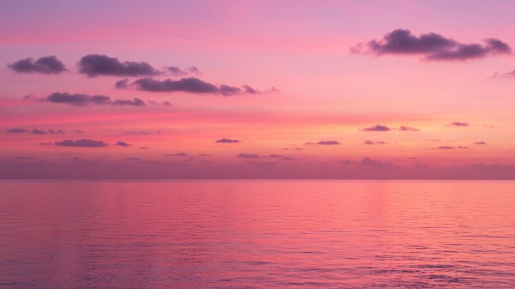 A vivid pink and soft-orange sunset sky over a calm ocean horizon