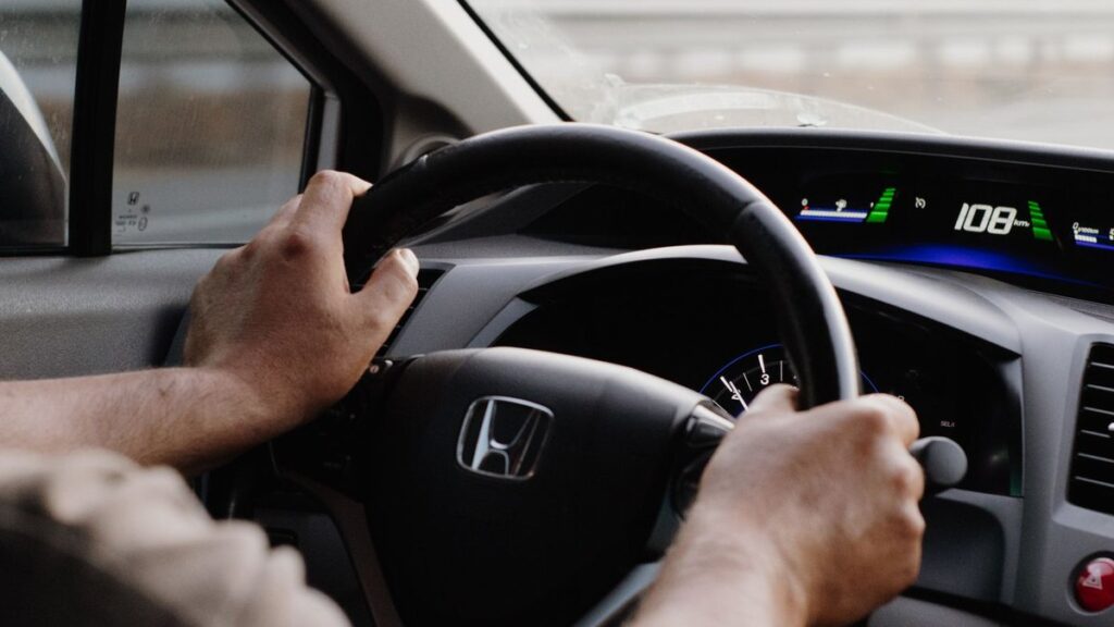 Driver's hands gripping the steering wheel of a moving car, the place where an acceleration shake is often felt first