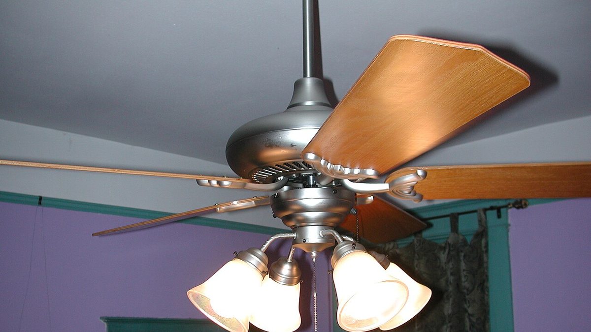 Close-up of a ceiling fan motor housing with wooden blades, light fixtures, and pull chains hanging below it