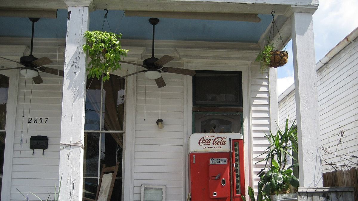 Two dark outdoor ceiling fans mounted on the blue ceiling of a white Southern porch with hanging plants