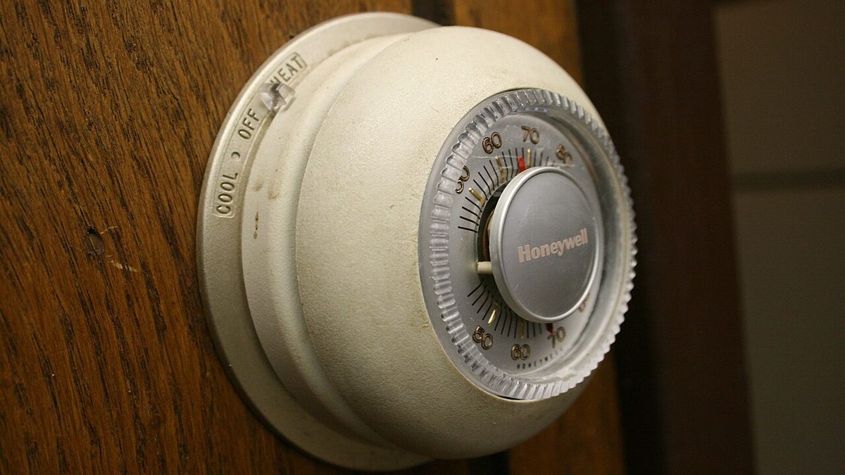 A classic round Honeywell wall thermostat with a Fahrenheit dial and a cool-off-heat switch, mounted on a wood-paneled wall