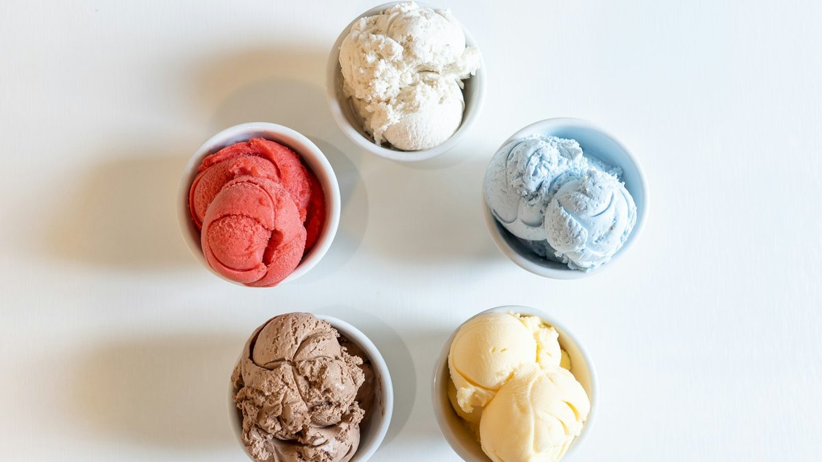 Overhead view of small bowls holding different flavor variations of blended frozen dessert, including a plain pale scoop, a chocolate-brown scoop, and a berry-red scoop