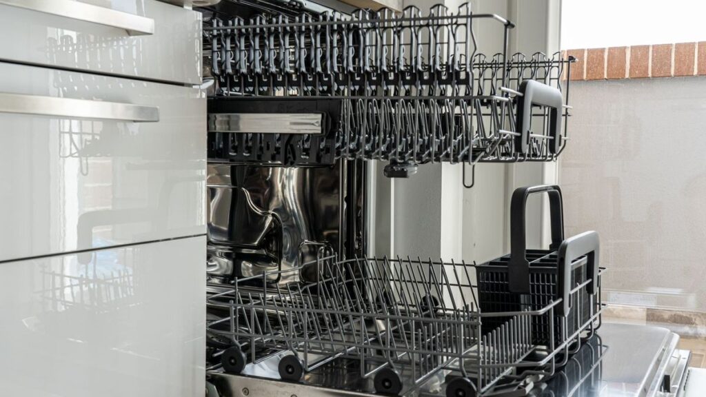 Open stainless steel dishwasher with empty racks pulled out in a bright modern kitchen