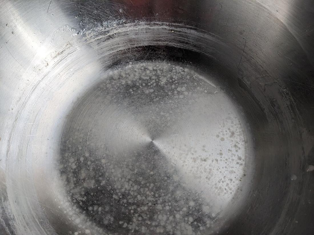 Chalky white limescale mineral deposit crusted on the bottom of a stainless steel pan