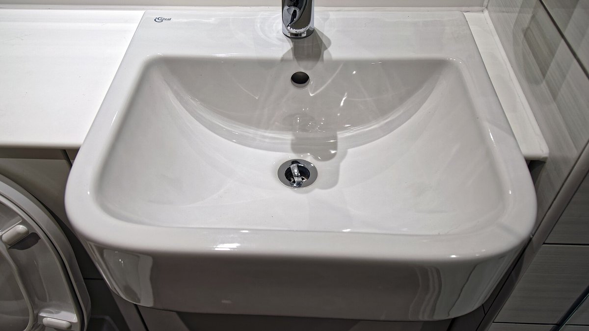 A clean white bathroom sink basin, whose drain biofilm can breed fruit flies or their look-alike drain flies
