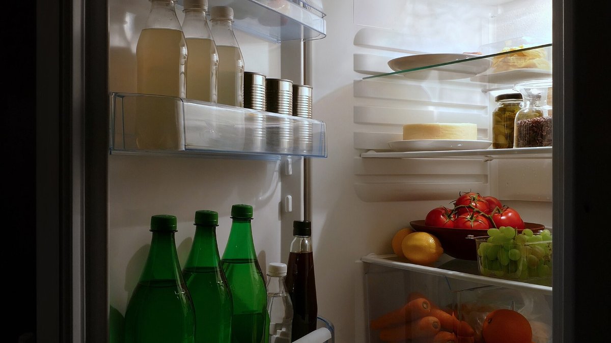 An open refrigerator at night full of produce including tomatoes, grapes, lemon and carrots, where fruit fly eggs can arrive on the skin of fruit
