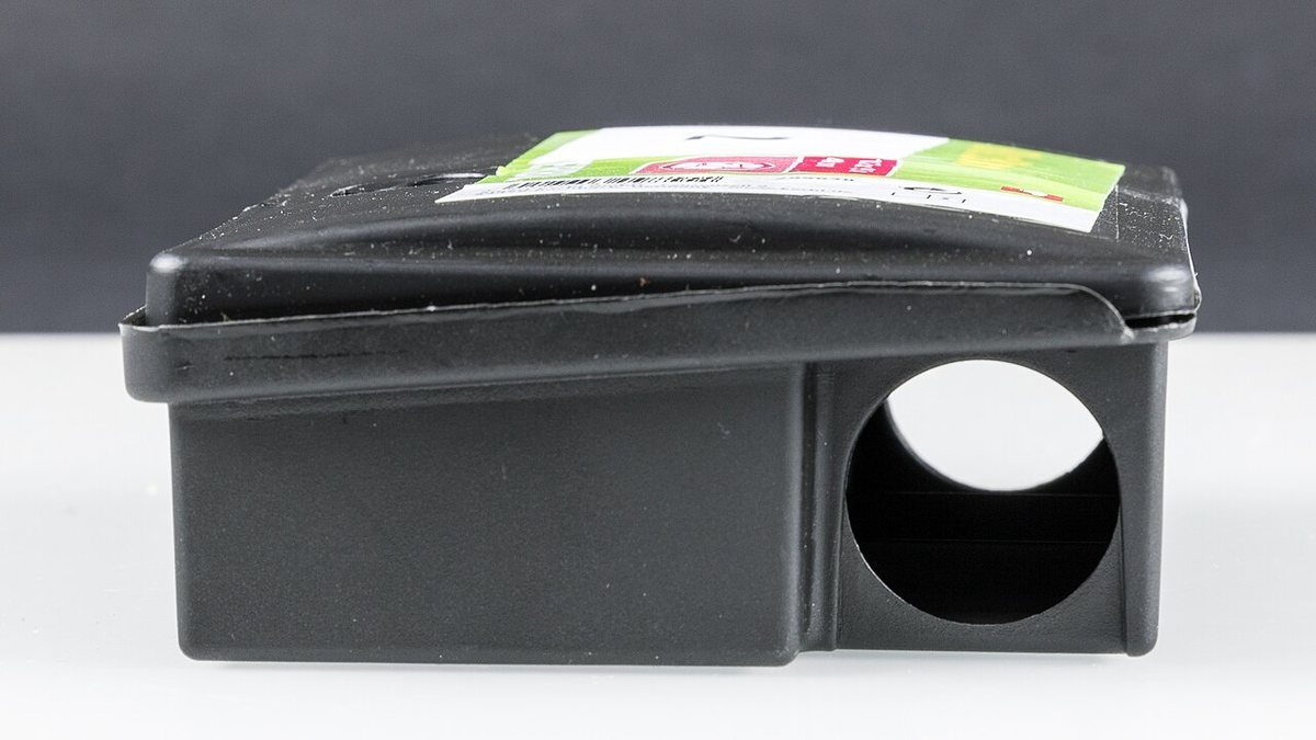 A black sealed plastic rodent bait station with a small entry hole, used to keep poison bait away from pets and children