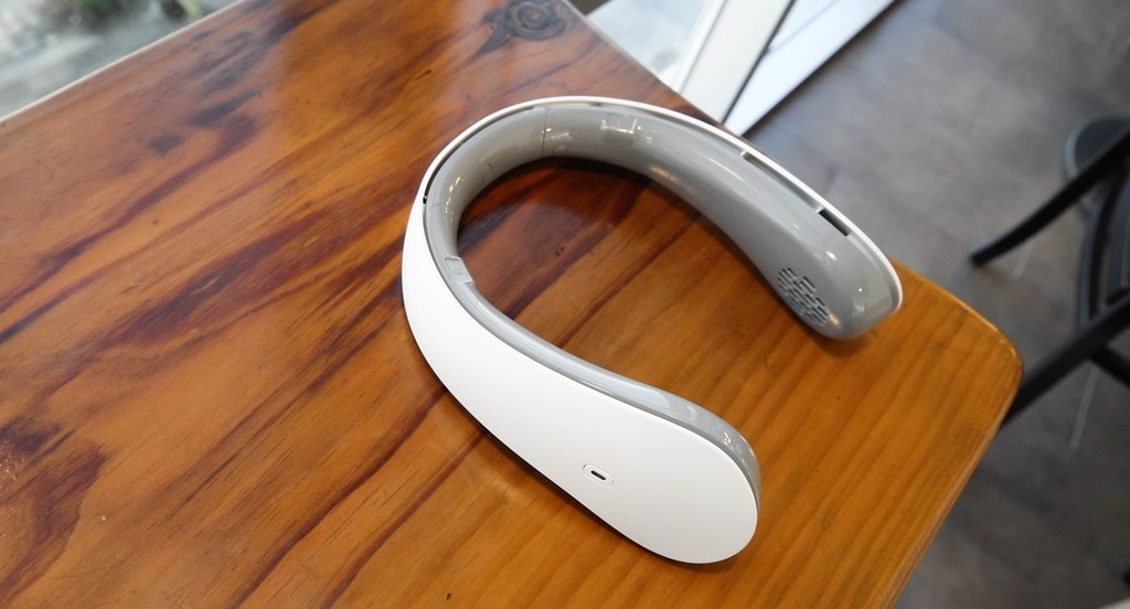White and grey bladeless neck fan lying on a wooden table, showing the U-shaped band and hidden air vents
