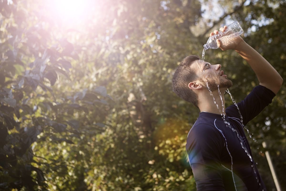 Man pouring water over his face to cool down in bright, intense summer sun