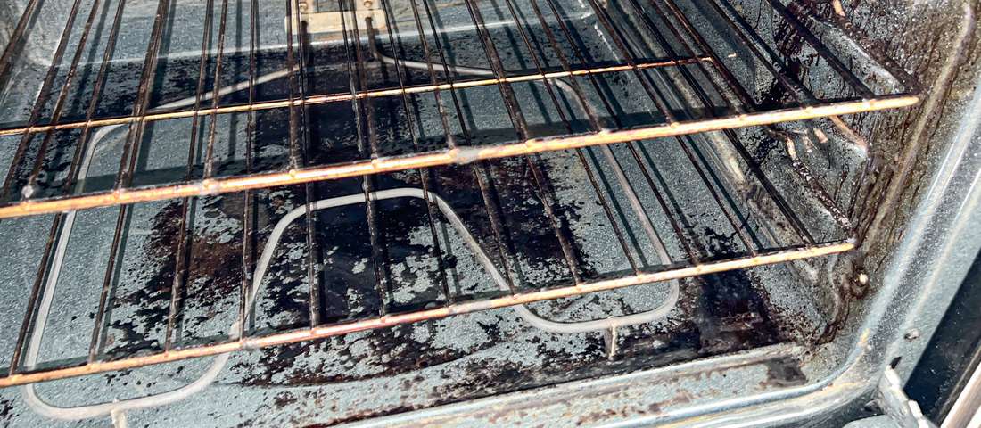 Close-up of the carbonized black crust baked onto the floor of a dirty oven, the level-three mess that needs an overnight soak