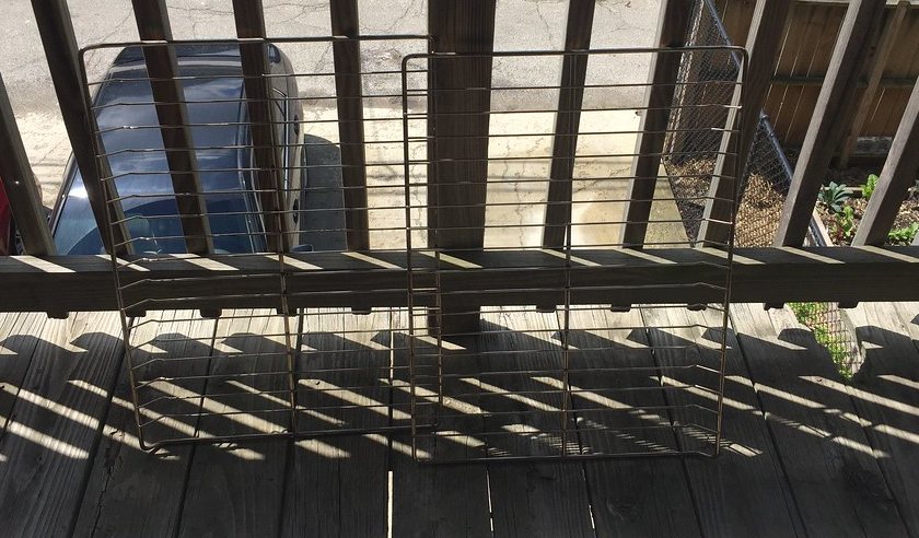 Two metal oven racks removed from the oven and standing outdoors, ready to be soaked and scrubbed