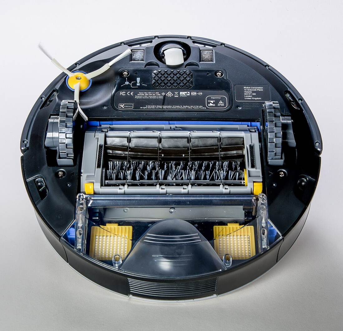 The underside of an older Roomba showing a stiff nylon bristle brushroll and a spinning side brush, the design pet hair wraps around
