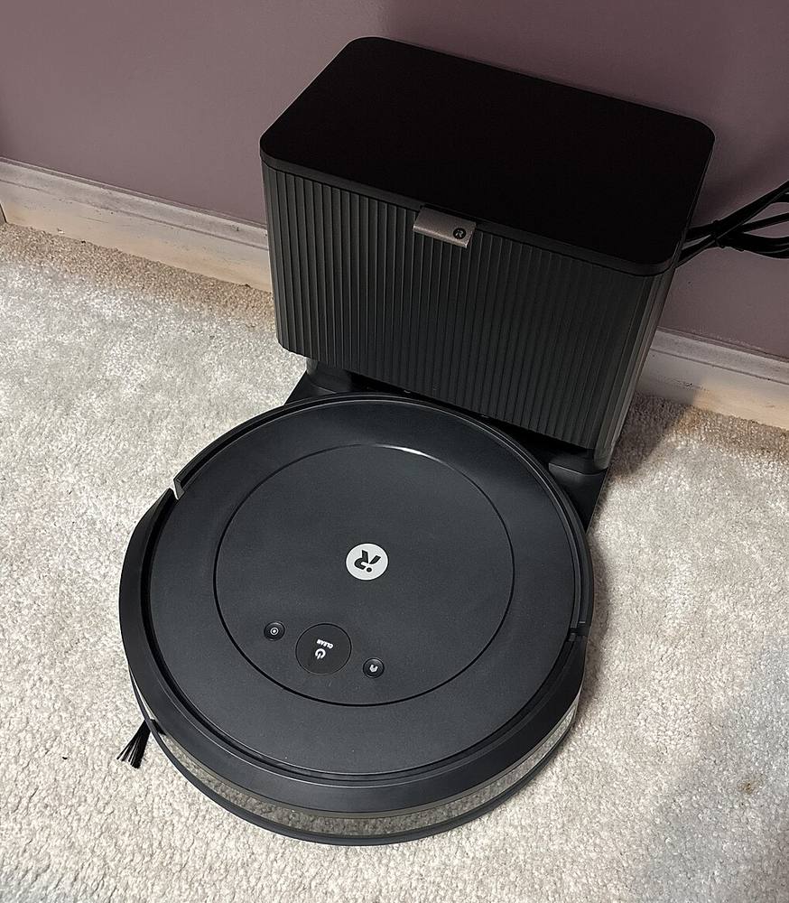 A Roomba robot vacuum in front of its tall black self-emptying base on carpet