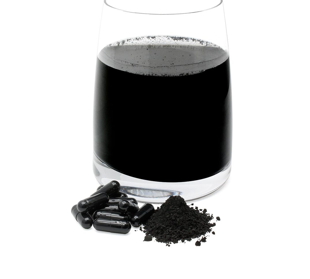 Activated charcoal shown as black powder, capsules, and a glass of charcoal water, the porous material that absorbs a wide range of odors