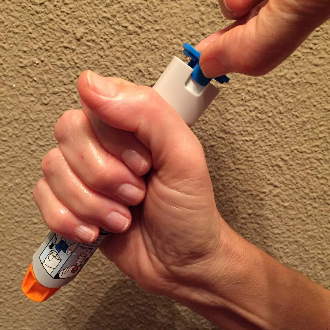 A person gripping an epinephrine auto-injector in a fist and pulling off its blue safety cap, the first step before injecting for a severe allergic reaction