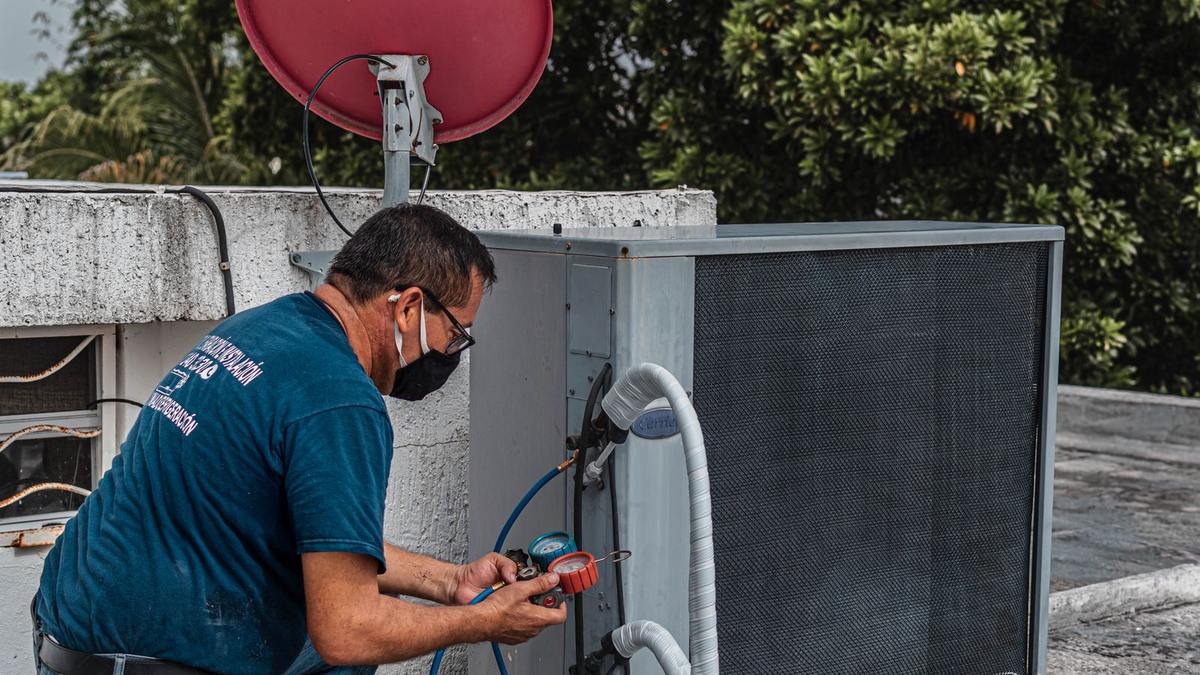 An HVAC technician connecting manifold pressure gauges to the service ports of a central air conditioner condenser